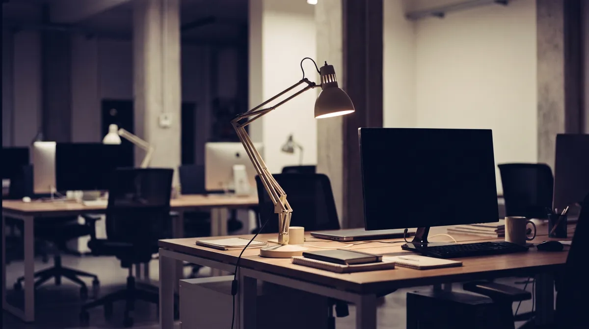 Scrivania moderna di notte con lampada accesa e monitor spento, ufficio open space in penombra