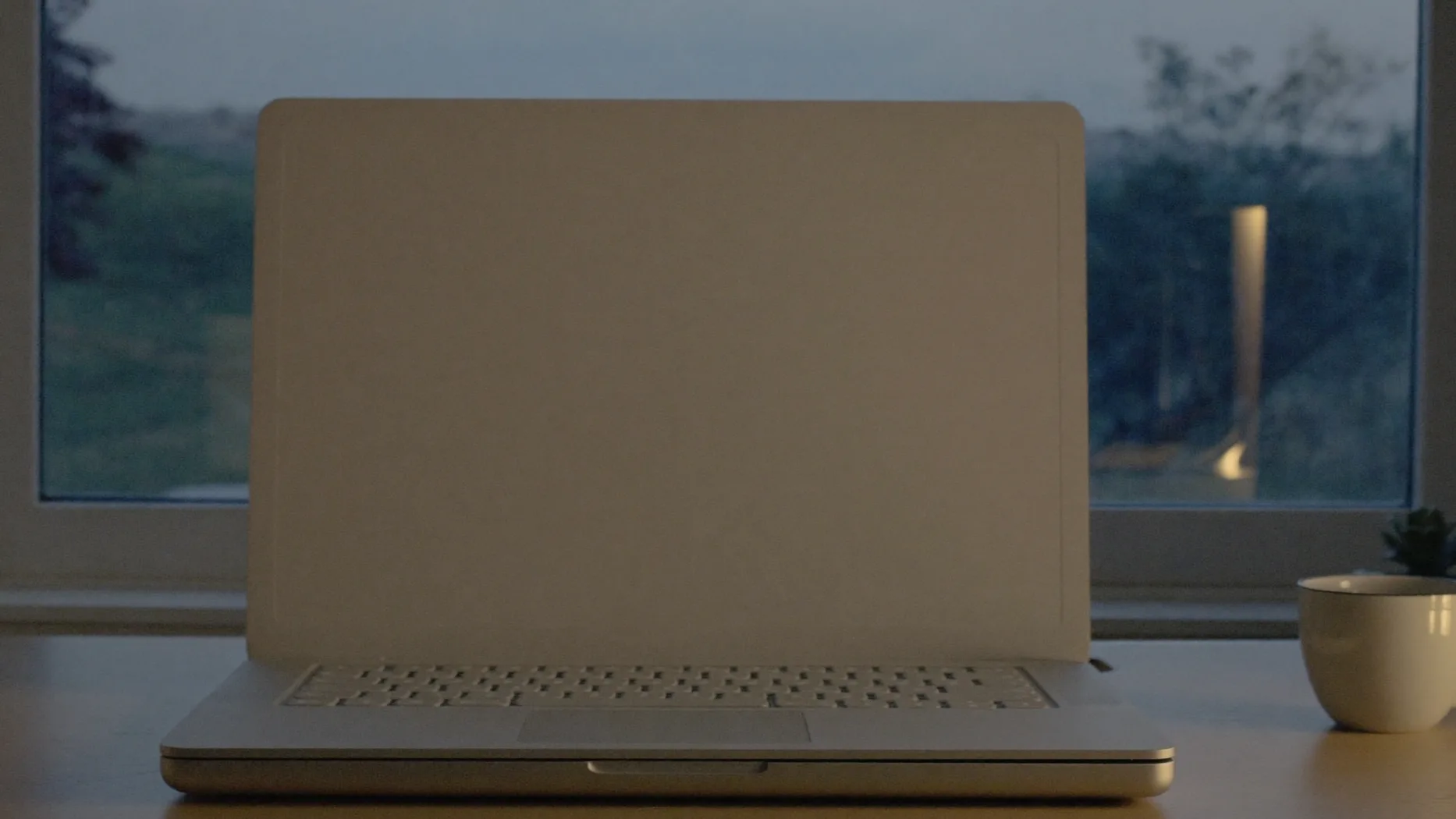 Laptop dal coperchio liscio su una scrivania in legno davanti alla finestra al crepuscolo