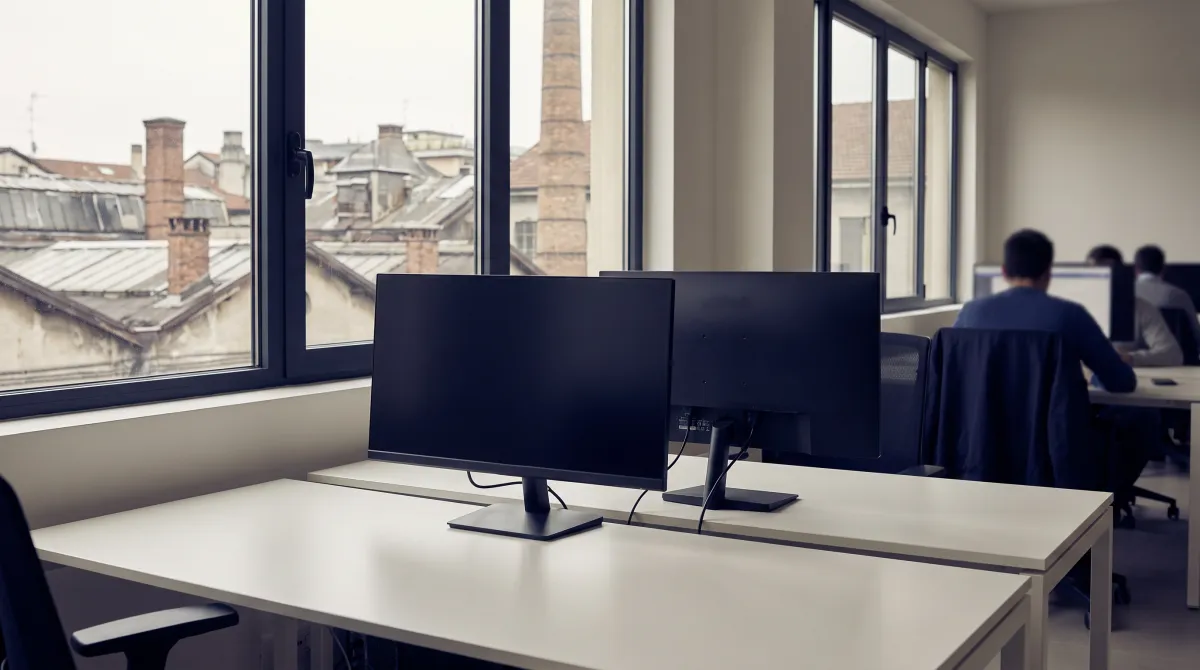 Ufficio software moderno con monitor piatti spenti e finestra sui tetti di un distretto industriale